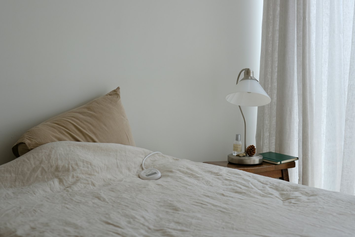 An electric blanket control sits on a made bedroom bed.