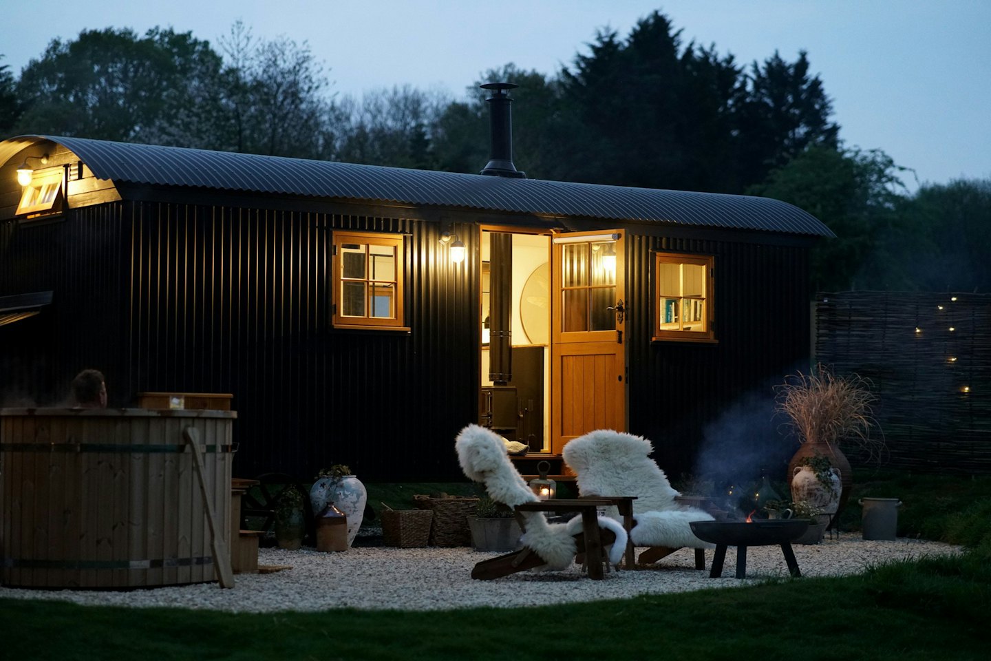 Person relaxing in a wooden hot tub beside a shepherd's hut.