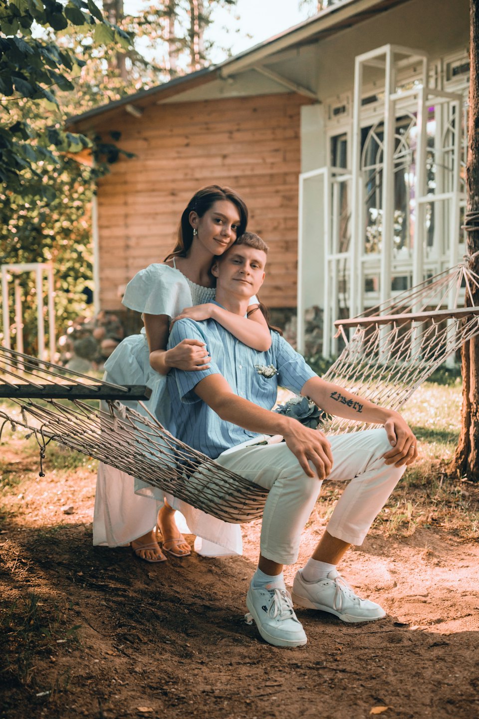 Couple embraces sitting in a hammock by a rustic cabin.