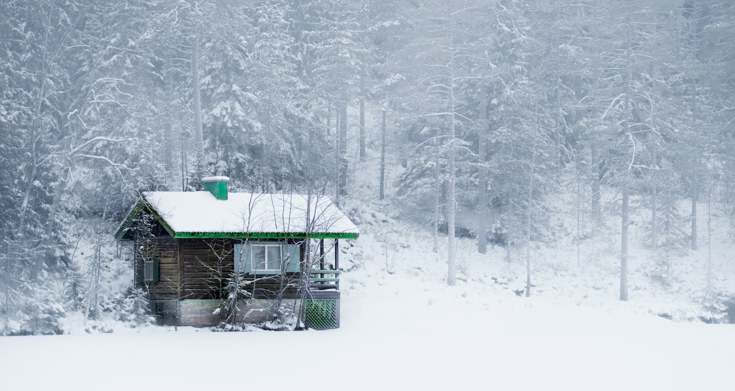 Snow-covered cabin with green roof in winter forest.