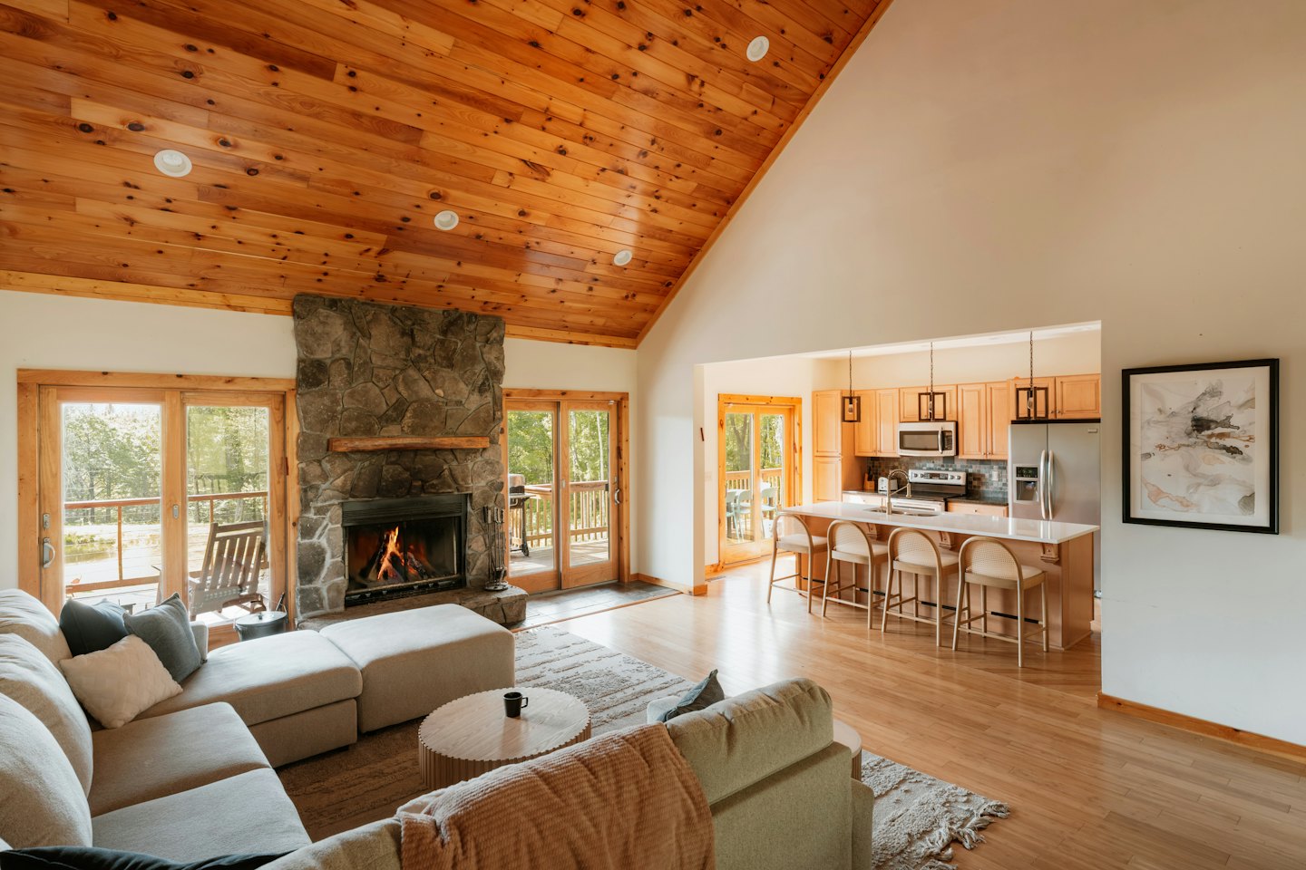 Modern cabin living room with stone fireplace and open kitchen.
